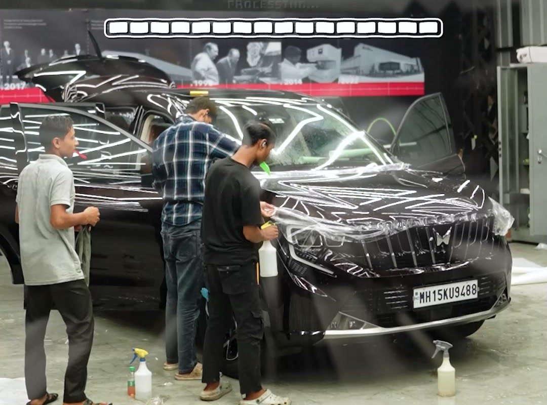 Two technicians laying film across a bonnet.